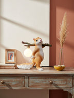 Clérachic squirrel table lamp on a distressed wooden console, with pampas grass in a vase and a rust-red wall behind.