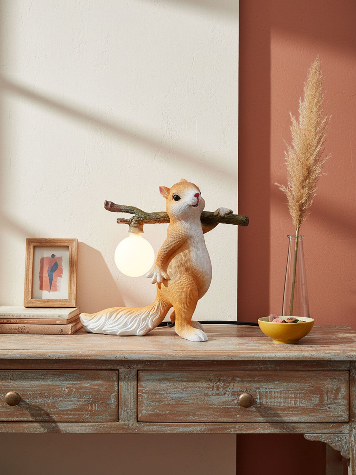 Clérachic squirrel table lamp on a distressed wooden console, with pampas grass in a vase and a rust-red wall behind.