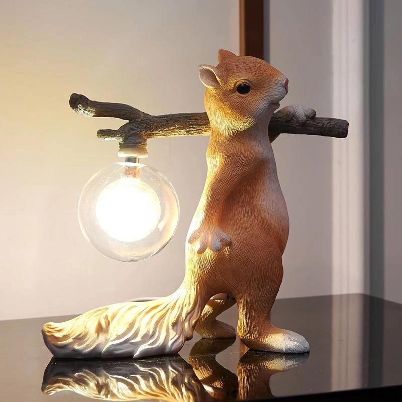 Browner version of the Clérachic squirrel lamp, lit with a warm clear glass globe on a glossy black surface.