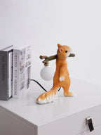A small Clérachic squirrel lamp on a white cabinet, beside two books and a loose black cable, with an unlit round bulb.