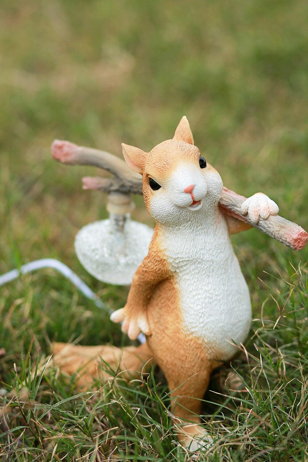 A Clérachic squirrel lamp on a grass lawn, looking at the camera, with a ribbed glass bulb hanging from the branch.