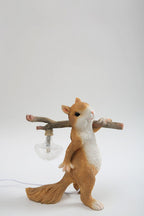 Side view of the Clérachic squirrel lamp on a grey backdrop, with its ribbed glass bulb hanging from the branch.