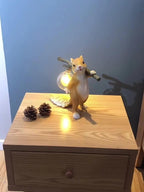 Clérachic squirrel lamp lit on a wooden bedside chest of drawers, next to two pine cones, against a blue wall.