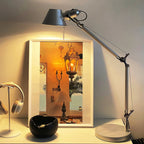 A Clérachic chrome desk lamp glowing warm against a framed picture, with a pair of headphones on a stand beside it.