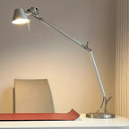Warm light from this Clérachic desk lamp, whose arm stretches over a white desk with a red desk mat.