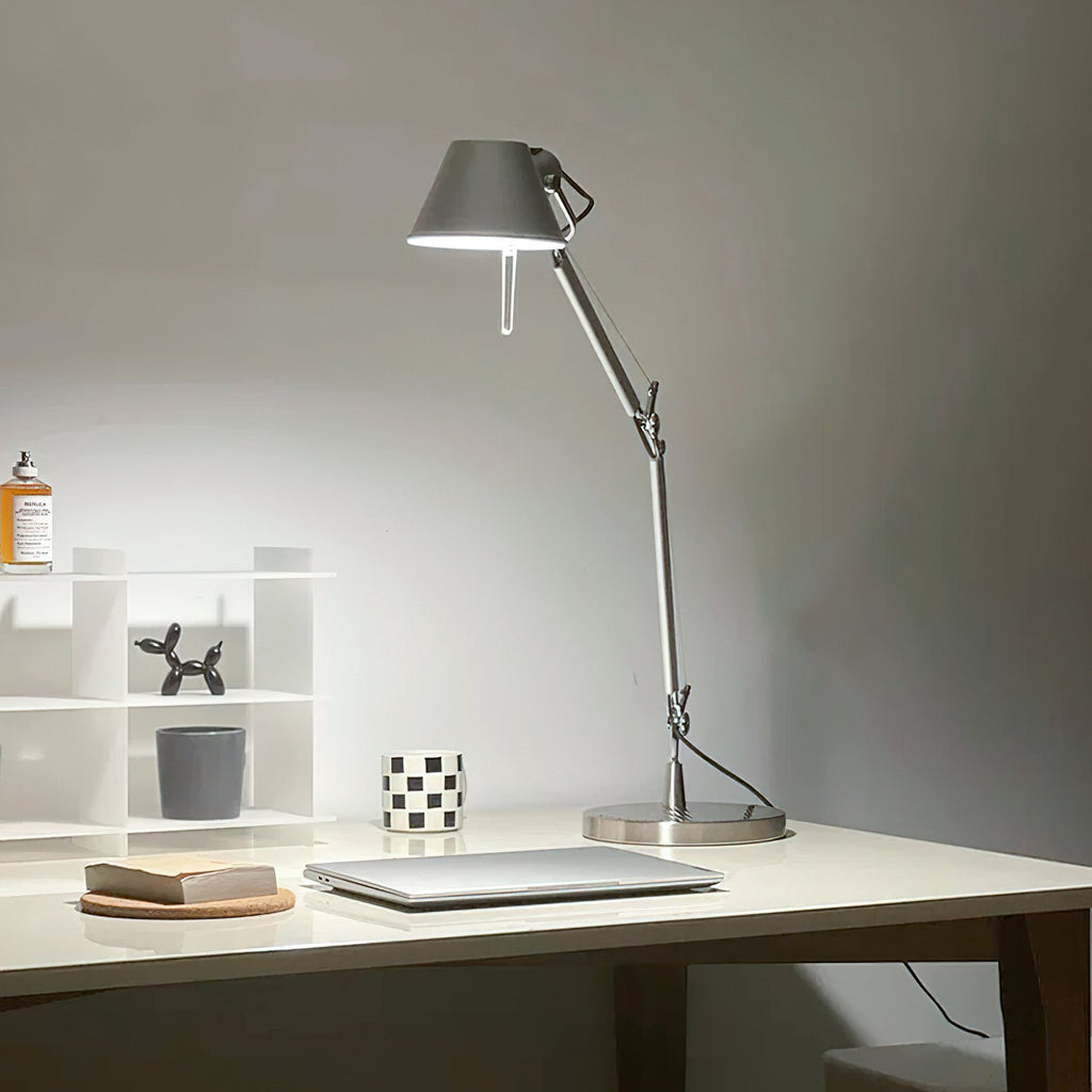 The Clérachic desk lamp lit on a white desk beside a small shelf, a laptop and a cork coaster.