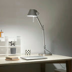 The Clérachic desk lamp lit on a white desk beside a small shelf, a laptop and a cork coaster.