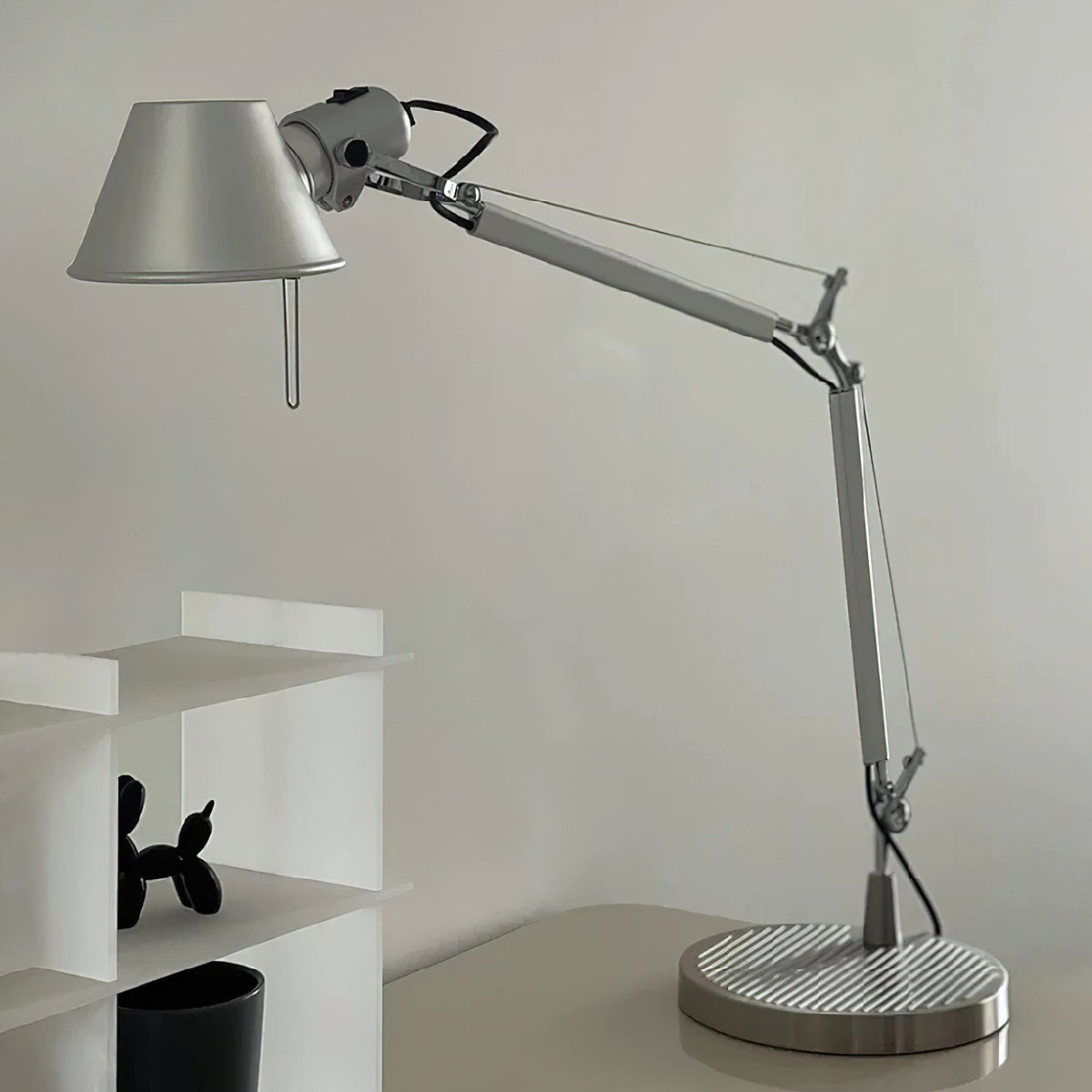 Close view of the conical shade, jointed arm and ridged base of this Clérachic desk lamp, with a small shelf nearby.
