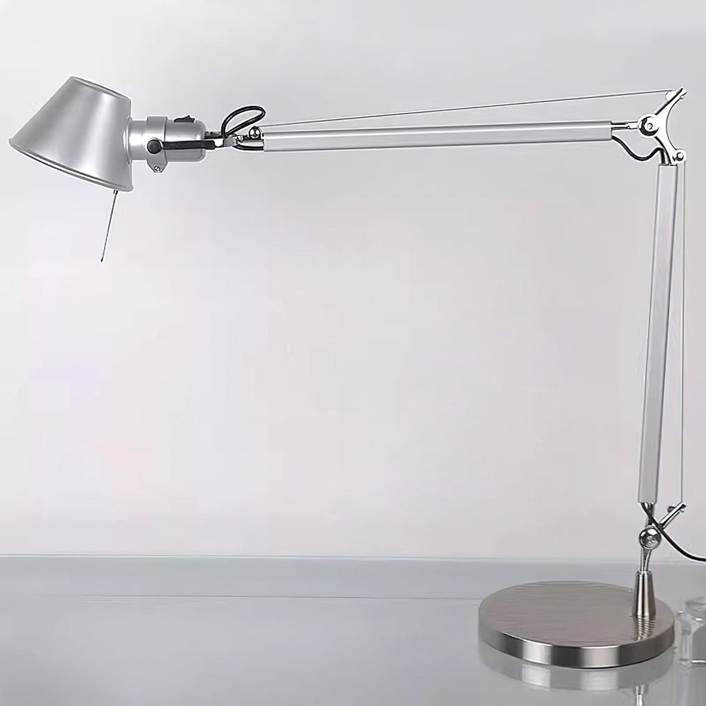 A Clérachic desk lamp with its arm extended, standing on a pale desk against a soft grey wall.