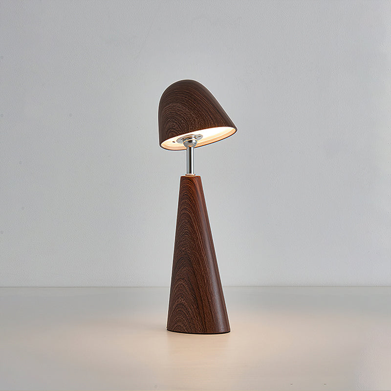 Walnut Clérachic table lamp with its dome shade tilted down, casting a warm circle of light on a pale grey backdrop.