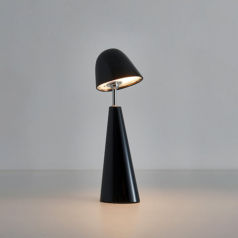 Black Clérachic table lamp with a dome shade tilted forward on a slim stem, lit against a soft grey wall.
