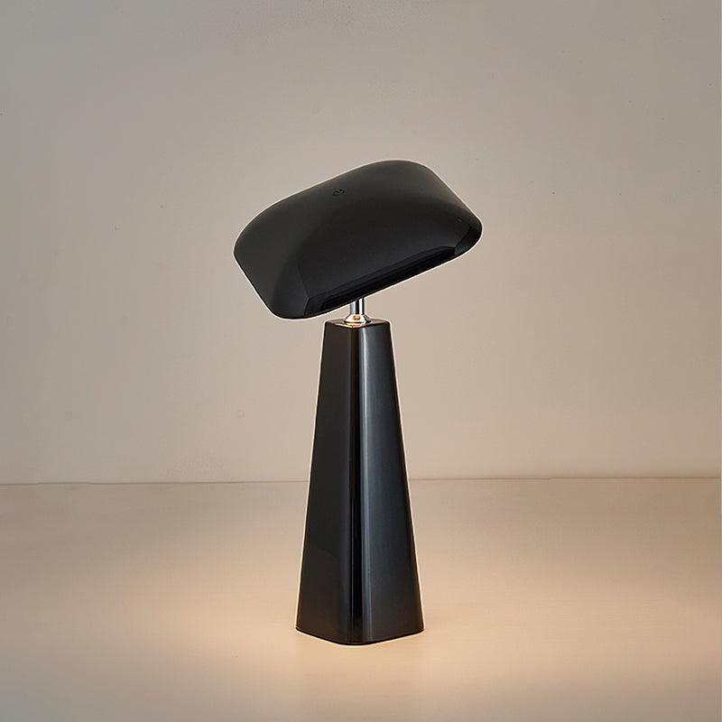 Black Clérachic table lamp with a glossy, tilted rounded-square shade on a tall tapered base, lit on a neutral backdrop.