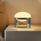 This Clérachic table lamp glows warm on a white bedside unit, its opal dome sitting over a chrome band with a curved cutout.