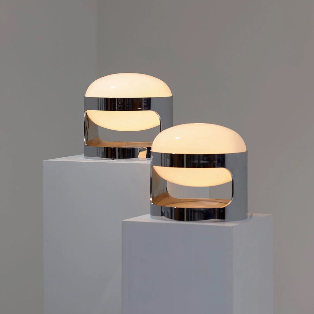 Two Clérachic table lamps with opal domes and chrome cutout bands, set on white plinths against a grey wall.
