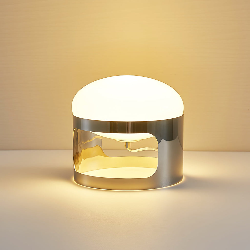 Close view of a lit Clérachic table lamp on a pale surface, with a warm glow from its opal dome and the chrome band.
