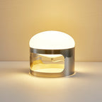 Close view of a lit Clérachic table lamp on a pale surface, with a warm glow from its opal dome and the chrome band.