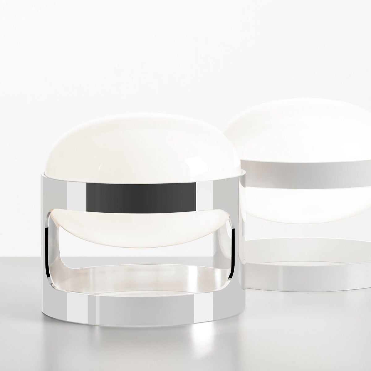 A chrome Clérachic table lamp in the foreground, with a white-finish version of the same shape softly blurred behind it.
