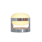 A lit Clérachic table lamp on a white backdrop, the chrome band reflecting colours from its surroundings.