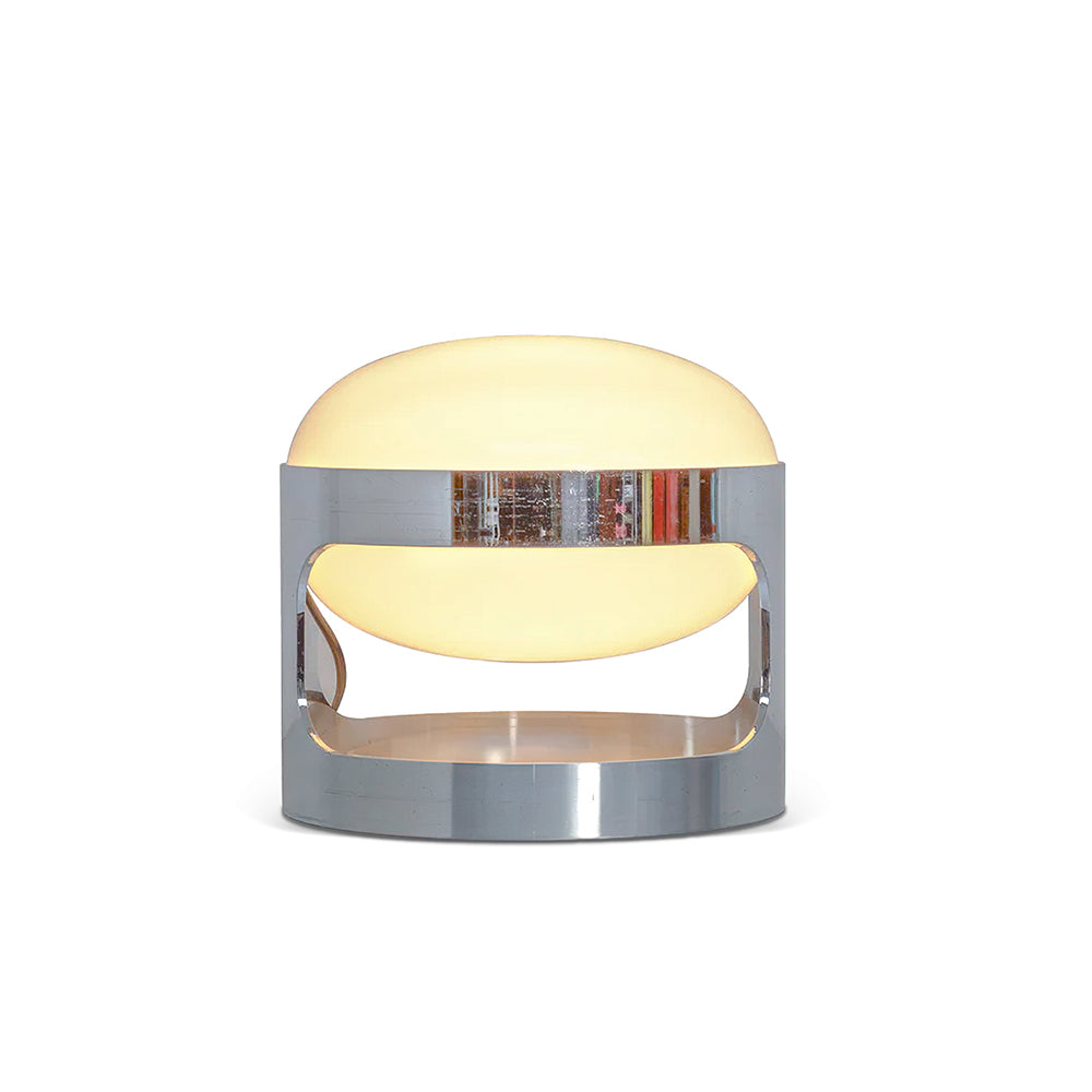 A lit Clérachic table lamp on a white backdrop, the chrome band reflecting colours from its surroundings.