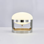 This Clérachic table lamp lit on a pale grey backdrop, its dome glowing soft white above the chrome band.