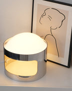 Clérachic table lamp on a white chest of drawers, lit, with a line-drawn portrait print leaning behind it.