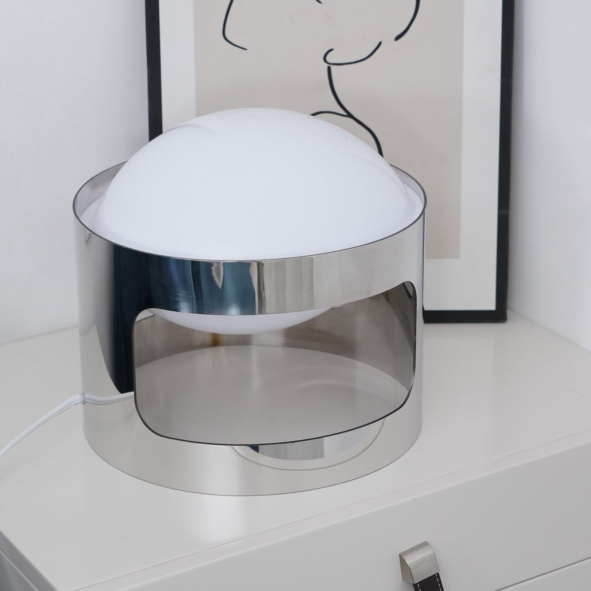 Clérachic table lamp unlit, close and angled, showing the white opal dome and the mirrored inside of its chrome band.