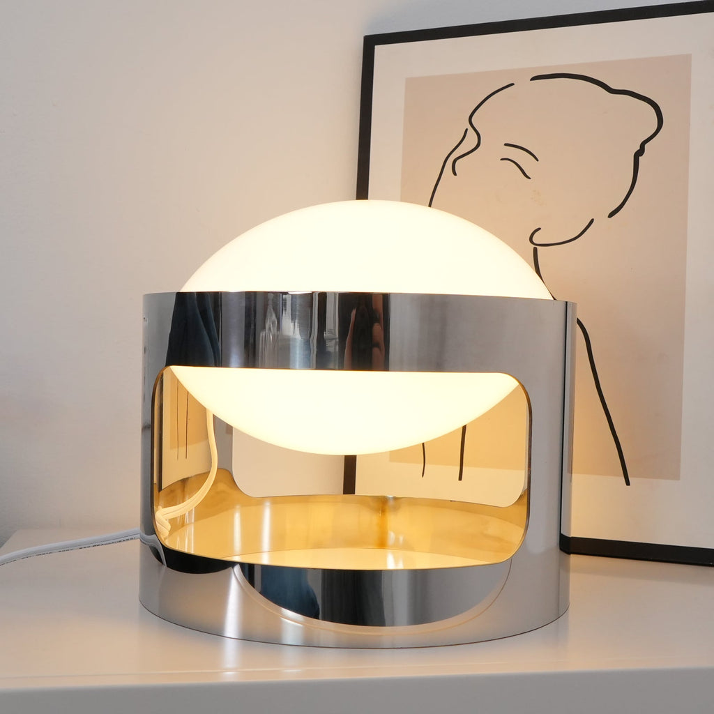 Close view of a lit Clérachic table lamp, with its opal dome above a chrome band that glows gold on the inside.