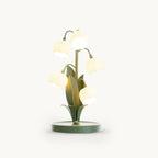 A Clérachic table lamp with five lit frosted white bell-flower shades on curved green stems, on a round green base, against a white backdrop.