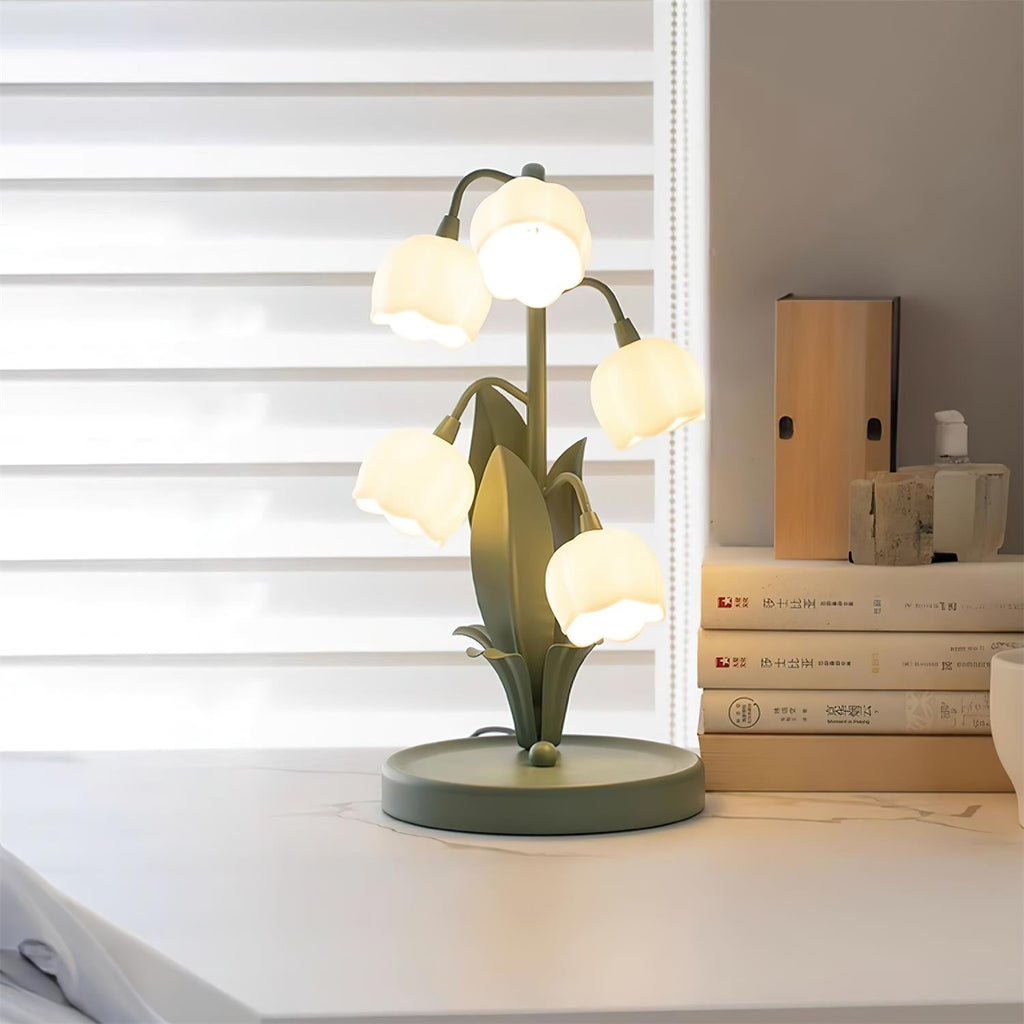 This Clérachic table lamp glows on a white desk beside a stack of books, with window blinds behind it.