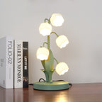 A lit Clérachic table lamp with bell-shaped shades stands on a dark wood shelf beside three upright books.