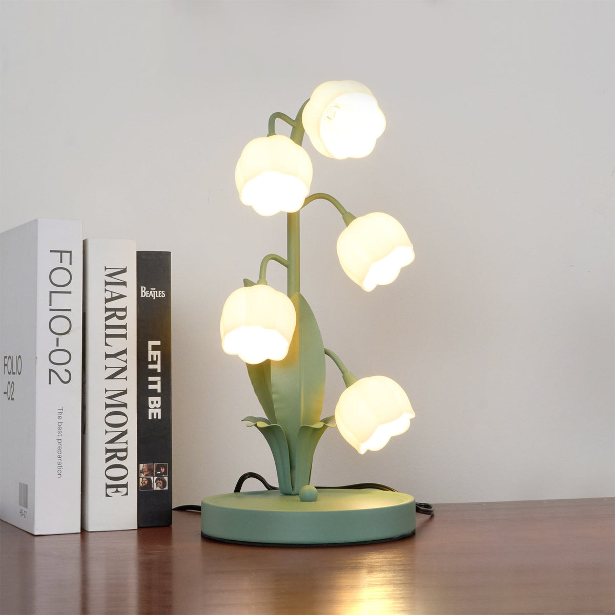 A lit Clérachic table lamp with bell-shaped shades stands on a dark wood shelf beside three upright books.
