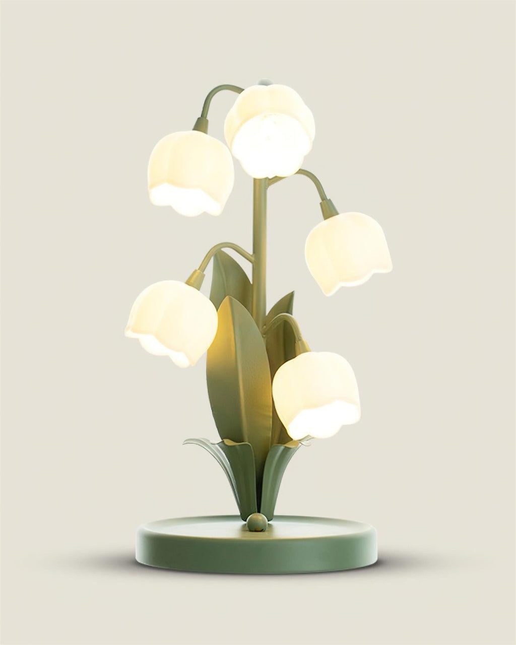 Close, slightly raised view of the Clérachic table lamp lit, with its round green base and bell shades glowing warm white.
