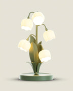 Close, slightly raised view of the Clérachic table lamp lit, with its round green base and bell shades glowing warm white.