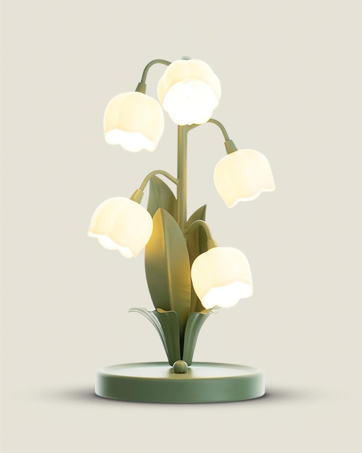 Close, slightly raised view of the Clérachic table lamp lit, with its round green base and bell shades glowing warm white.