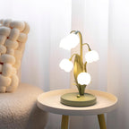 Clérachic table lamp lit on a small round white tray table with a chunky cream knitted cushion and white curtains behind it.