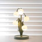A lit Clérachic table lamp on a white marble surface, with its bell shades glowing against striped window blinds.