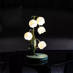This Clérachic table lamp glows in a dark room, standing on a dark glass tabletop with its green base just visible.