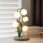 A Clérachic table lamp lit on a marble desk beside a pile of books and a small heater, with blinds and a dark curtain behind.