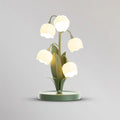 Clérachic table lamp lit on a light grey backdrop, its five bell shades glowing above the round green base.