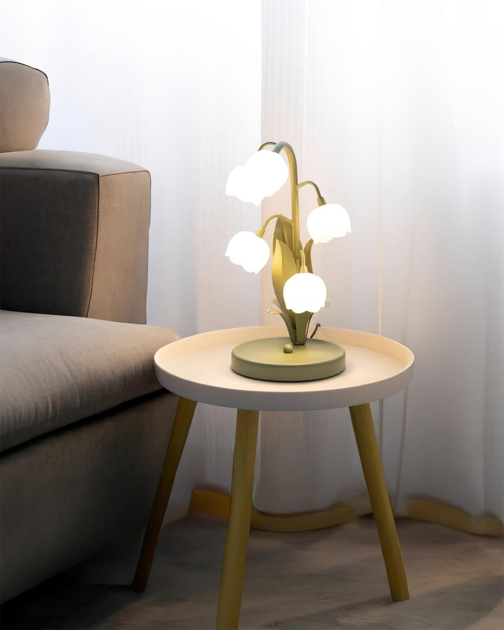 Wide view of a Clérachic table lamp on a small round side table beside a grey sofa, with sheer curtains behind.