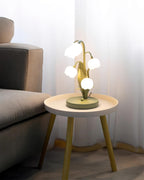 Wide view of a Clérachic table lamp on a small round side table beside a grey sofa, with sheer curtains behind.