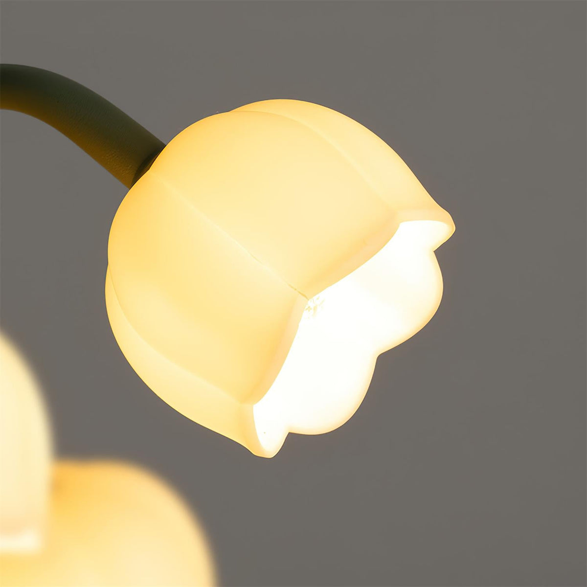 Close view of one bell shade of this Clérachic table lamp, lit warm yellow against a dark grey backdrop.