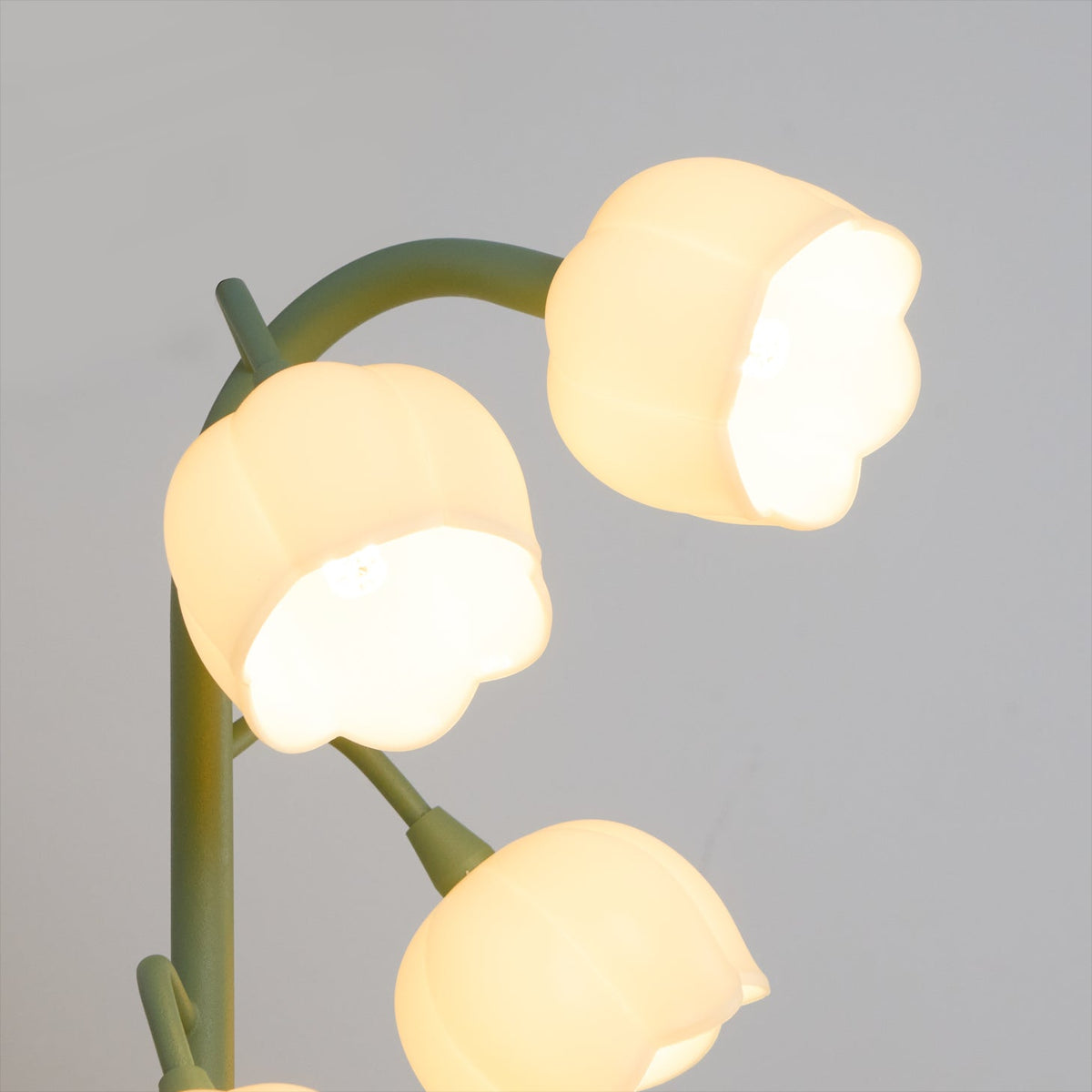 Close view of three lit bell shades on slim curved stems of this Clérachic table lamp, against a pale grey wall.