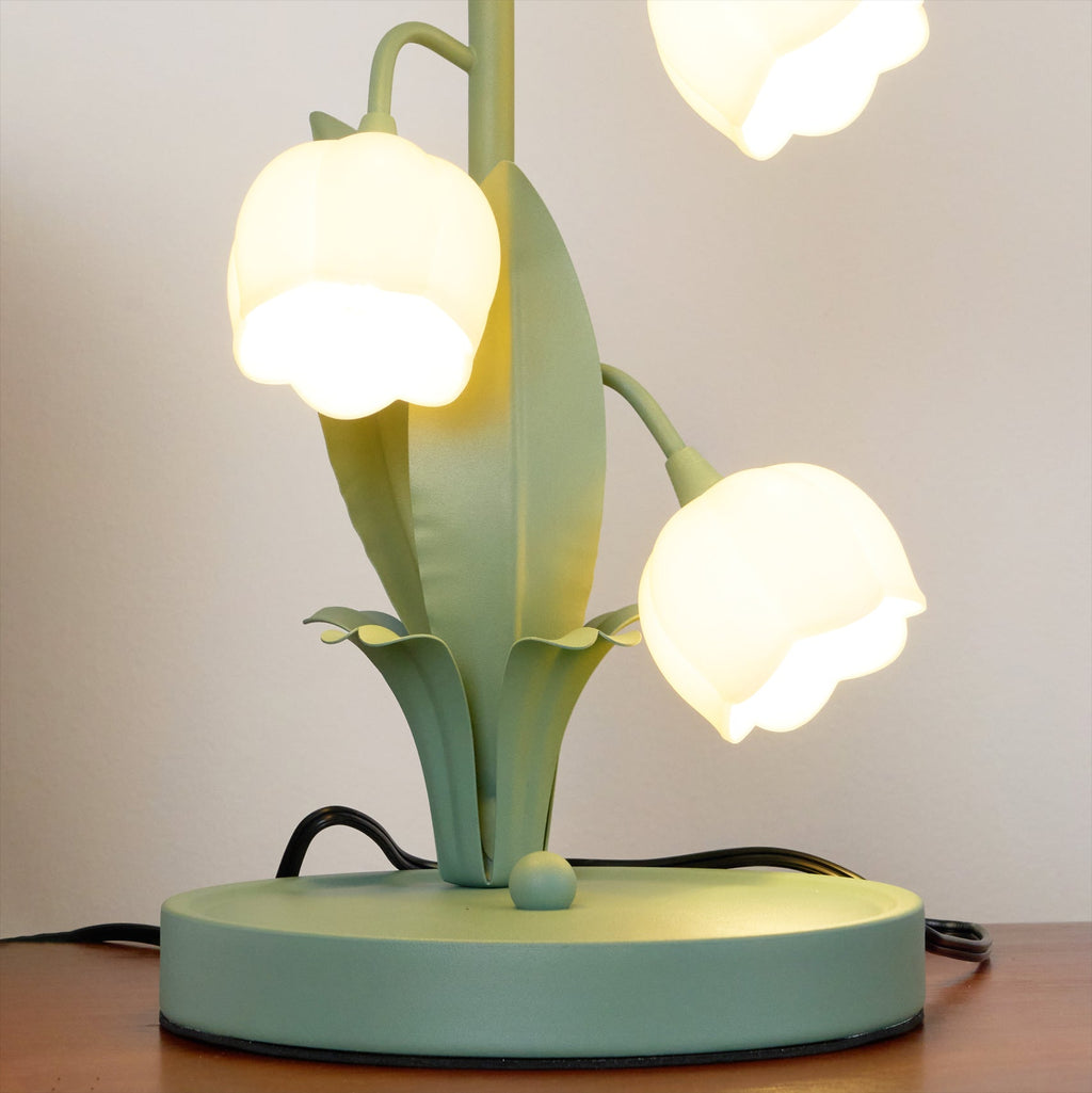 Lower half of this Clérachic table lamp, lit, showing the round green base, the leaf blades and two bell shades.