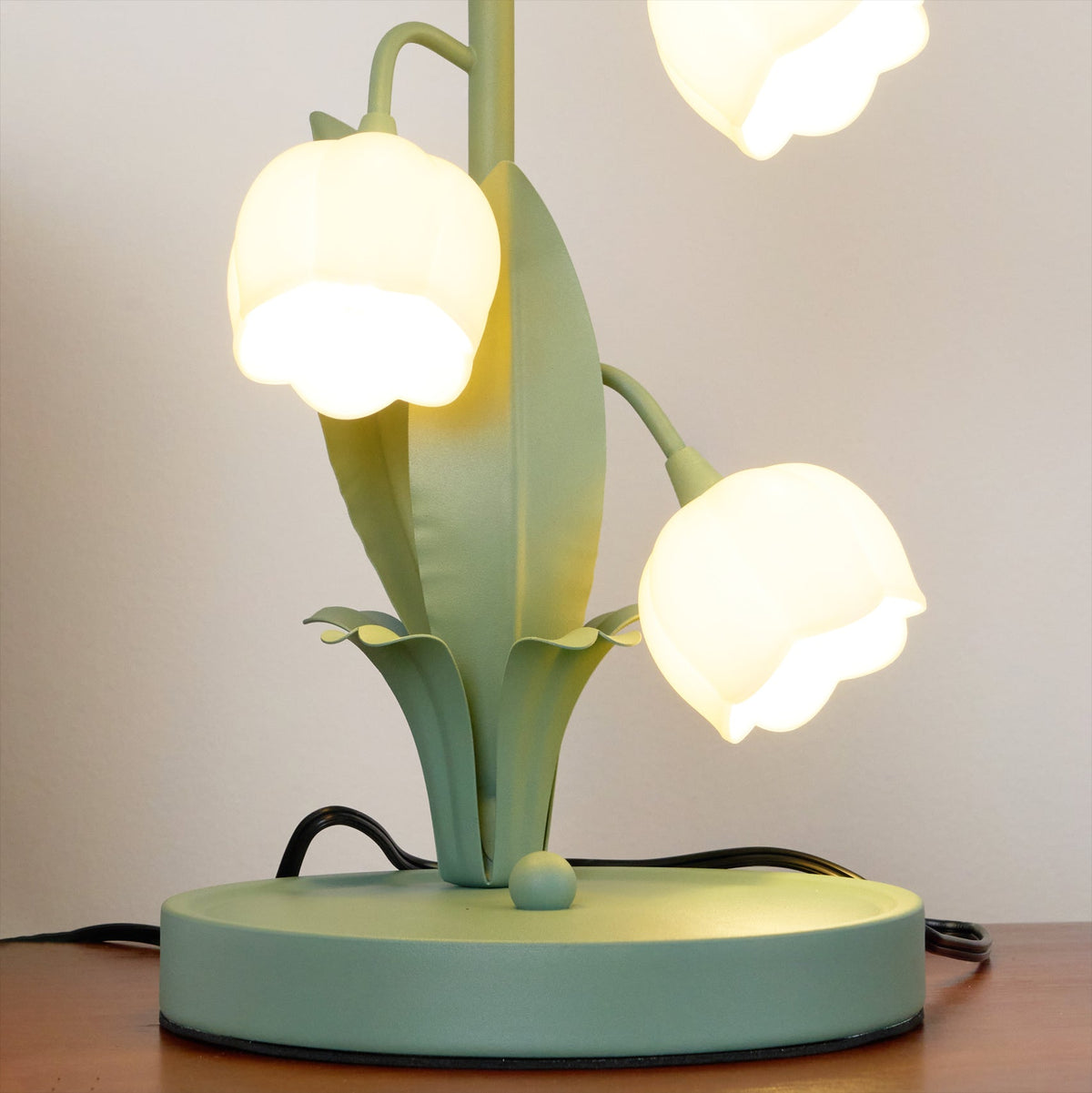 Lower half of this Clérachic table lamp, lit, showing the round green base, the leaf blades and two bell shades.