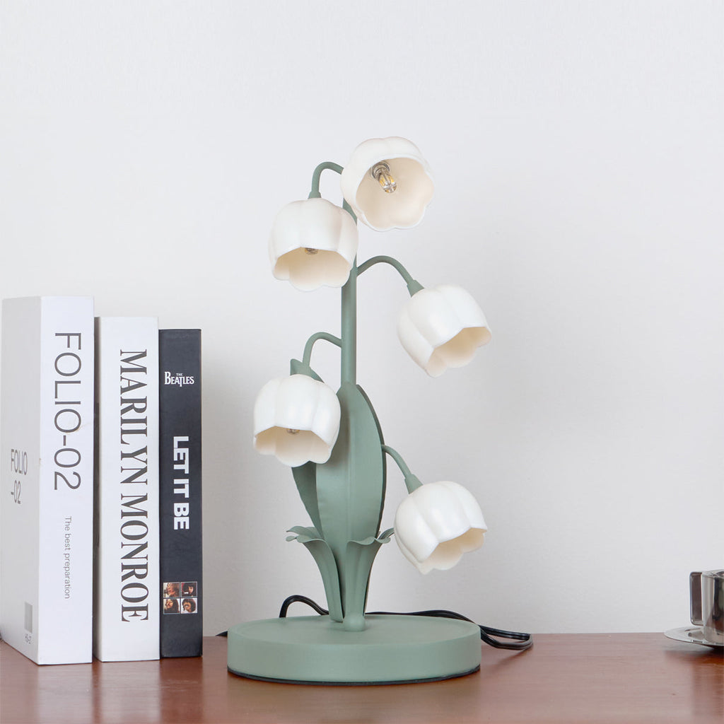 This Clérachic table lamp, switched off, stands on a wooden shelf beside books, its white bell shades on green stems.