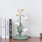This Clérachic table lamp, switched off, stands on a wooden shelf beside books, its white bell shades on green stems.
