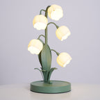 Clérachic table lamp lit on a pale grey backdrop, with five bell shades on curved stems above a round green base on a white surface.