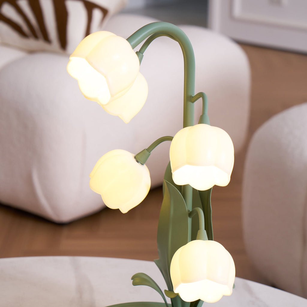 Close view of the top of this lit Clérachic table lamp, with warm glowing bell shades on arched green stems above cream furniture.