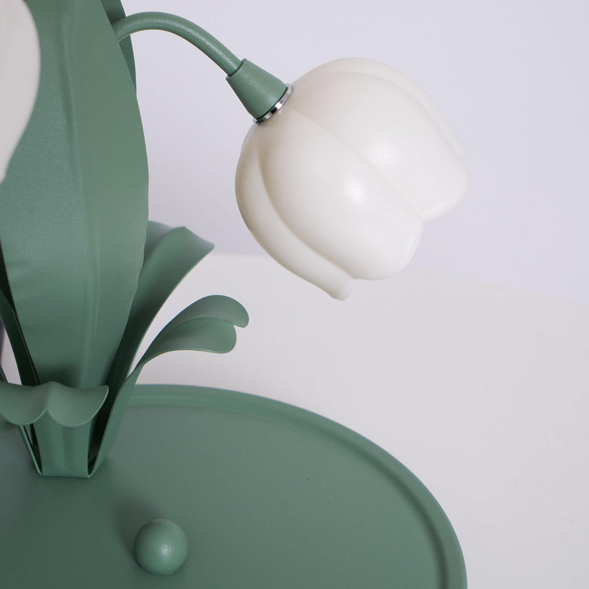 Close view of a bell shade and the leaf blades on the green base of this unlit Clérachic table lamp.